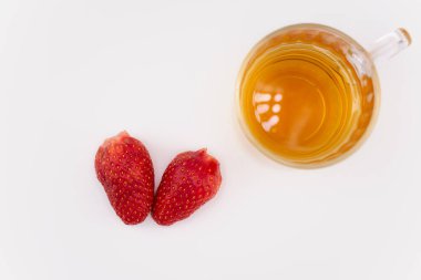 Canlı çileklerin yanında berrak bir bardak yeşil çay sükunet ve sağlıklı bir ferahlatıcı çağrıştırıyor. Detoks içeriği, rahat yaşam tarzı veya temiz yemek blogları için ideal