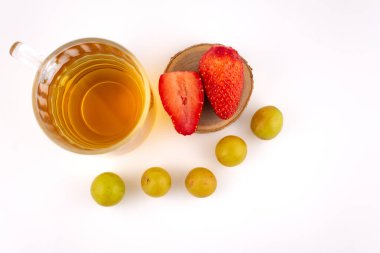 Taze çilek ve yeşil üzüm taşıyan ahşap bir bardak altının yanında altın bitkisel çay bulunan cam bardak. Düzenleme, zarif bir sunumla sağlık ve beslenme üzerine odaklanılmasını öneriyor..