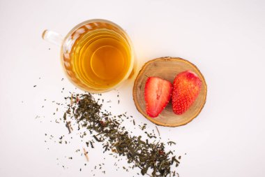 Canlı çilekler ve dağınık çay yapraklarının yanında berrak bir bardak yeşil çay sükunet ve sağlıklı bir ferahlatıcı çağrıştırıyor. Detoks içeriği, rahat yaşam tarzı veya temiz yemek blogları için ideal