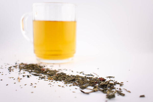 Крупный план включает в себя прозрачный стакан яркого зеленого чая, с рыхлыми листьями, изящно разбросанными под ним, вызывая чувство спокойствия и здорового снисхождения. Идеально подходит для хорошего самочувствия, детокса или заботливой жизни