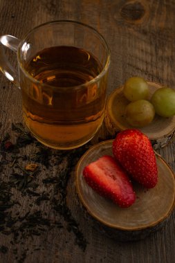 Bir bardak yeşil çay, taze çilek ve sulu üzümler sağlıklı bir hoşgörü ve saflık hissi uyandırıyor. Temiz yemek, sağlıklı yemek tarifleri veya düşünceli yaşam tarzı içeriği için ideal