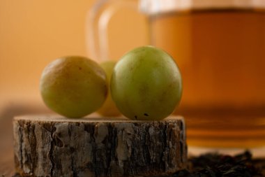 Bu sanatsal kompozisyonda bir bardak yeşil çay, gevşek çay yaprakları ve kırsal ahşap üzerinde taze yeşil üzümler bulunur. Bu da doğal bir refah ve hoş bir basitlik hissi uyandırır. Sağlık blogları, bilinçli yaşam ya da içecek endüstrisi içeriği için ideal