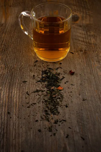 Sadelikte sükuneti bul! Dağılmış çay yaprakları ile kırsal bir ahşap yüzeye odaklanmış cam bardak dolusu yeşil çay, sakinlik ve doğal saflığı çağrıştırıyor. Sağlık, dikkatli yaşam ya da içecek temaları için idealdir.