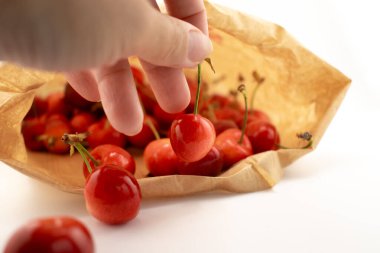 Yakın plan çekimde, taze, olgun bir kiraz seçmek için bir kese kağıdına uzanan bir el yakalıyor ve doğal bir iyilik hissi uyandırıyor. Organik gıda, çiftçi pazarı veya çevre dostu yaşam tarzı içeriği için ideal