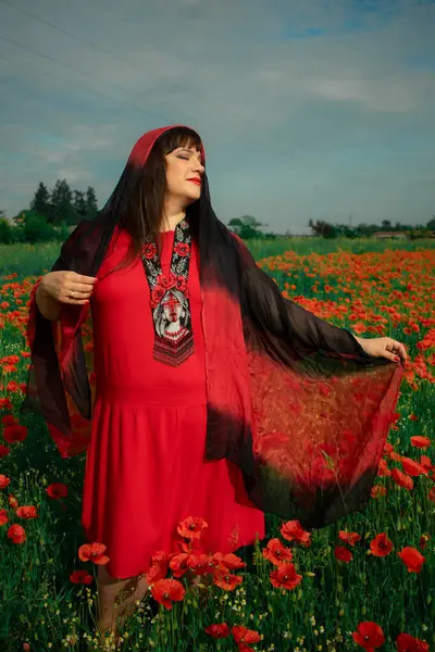 Kırmızı elbiseli bir kadın ve canlı gelinciklerle dolu bir tarlada siyah ve kırmızı bir başörtüsü. Huzur, doğa ile bağlantı ve ruhsal huzur duygusu. Farkındalığın teması ve doğal güzellik.