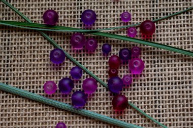 Kırsal bir çuval bezi dokusunda yeşil aksanlı canlı mor boncuklar. Sanat projeleri için mükemmel, DIY, veya sanatsal geçmiş, yaratıcı tasarımlar, mücevherler