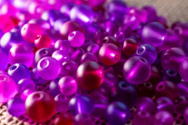 Şeffaf mor ve pembe boncuklardan oluşan renkli bir şelale dokulu bir yüzeyde ışığı yakalıyor, bir sonraki yaratıcı girişimin için hazır. DIY içeriği, mücevher veya soyut arka planlar için harika