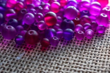 Şeffaf mor ve pembe boncuklardan oluşan renkli bir şelale dokulu bir yüzeyde ışığı yakalıyor, bir sonraki yaratıcı girişimin için hazır. DIY içeriği, mücevher veya soyut arka planlar için harika