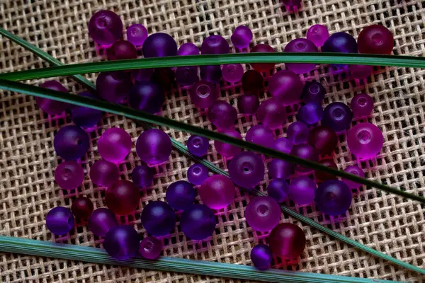 Kırsal bir çuval bezi dokusunda yeşil aksanlı canlı mor boncuklar. Sanat projeleri için mükemmel, DIY, veya sanatsal geçmiş, yaratıcı tasarımlar, mücevherler