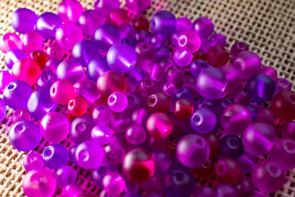 Şeffaf mor ve pembe boncuklardan oluşan renkli bir şelale dokulu bir yüzeyde ışığı yakalıyor, bir sonraki yaratıcı girişimin için hazır. DIY içeriği, mücevher veya soyut arka planlar için harika