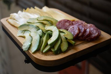Peynir, salam ve avokado ile nefis bir abur cubur tahtası, şık desenli bir bardakla eşleştirilmiş. Yemek blogları için mükemmel, eğlenceli, rahat anlar, evde dinlenme, sosyal toplantılar, ya da hafif yemekler