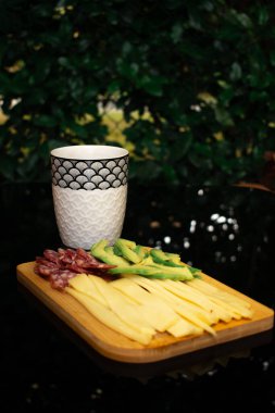 Peynir, salam ve avokado ile nefis bir abur cubur tahtası, şık desenli bir bardakla eşleştirilmiş. Yemek blogları için mükemmel, eğlenceli, rahat anlar, evde dinlenme, sosyal toplantılar, ya da hafif yemekler