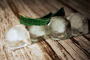 Taze nane yaprakları ve parlak buz küpleri görünür su damlacıkları olan ahşap bir yüzeyde dinleniyor. Bu görüntü ferahlatıcı bir serinlik ve doğal malzemeler hissi veriyor, içecek ve yaz temaları için mükemmel..