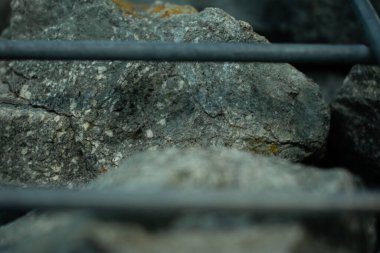 Metal bir kafesin içinde bulunan koyu renkli kayaların yakın plan görüntüsü. Doğal kabalık, modern peyzaj ve mimari dokular. İnşaat, bahçe tasarımı veya soyut doğa temaları için.