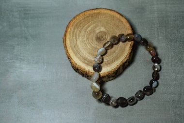 Kırsal ahşap bir dilimde zarif bir şekilde sergilenen, doğal tonlar ve desenler içeren topraksı agat boncuklu bir bilezik. Doğal mücevher, ruhani aksesuarlar ve bohem tarzı temalar için mükemmel..