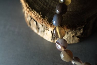 Kırsal ahşap bir dilimde zarif bir şekilde sergilenen, doğal tonlar ve desenler içeren topraksı agat boncuklu bir bilezik. Doğal mücevher, ruhani aksesuarlar ve bohem tarzı temalar için mükemmel..