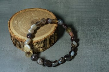 Kırsal ahşap bir dilimde zarif bir şekilde sergilenen, doğal tonlar ve desenler içeren topraksı agat boncuklu bir bilezik. Doğal mücevher, ruhani aksesuarlar ve bohem tarzı temalar için mükemmel..