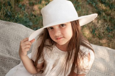 Geniş kenarlı şapkalı genç bir kız piknik battaniyesinde, elinde sepetle, dışarıda geçen bir yaz gününün masum neşesini ve rahatlamış ruhunu somutlaştırıyor..