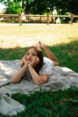 Hayalperest genç bir kız, gölgenin altındaki piknik battaniyesine uzanmış başını ellerinin arasına almış dinleniyor. Sakin, hayal gücü ve basit çocukluk sevinciyle dolu huzurlu bir yaz günü..