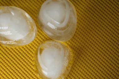 Bulutlu merkezli üç parlak yarı şeffaf taş örülmüş sarı bir yüzey üzerinde duruyor. Basit, sakin ve organik güzellik temaları için ideal minimalist, doğadan esinlenilmiş bir sahne..