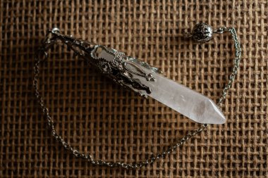 Süslü metal işlemeli bir kuvars kristal sarkacı çuval bezinde duruyor. Kehanette ve enerji çalışmalarında kullanılan sahne mistisizmi, ritüeli ve ruhani sembolizmi çağrıştırıyor..