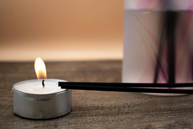 Siyah sazlıklar ve altın kapaklı buzlu bir cam kırıcı, tahtanın üzerinde yanan bir tealenin yanında oturur. Sıcak, rahatlatıcı, aromaterapi, rahatlama ve minimalist sağlık çağrıştıran bir kurulum..