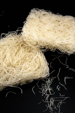 Koyu bir yüzey üzerinde beyaz pirinç eriştesi yığını duruyor. İnce, parlak iplikler, Asya yemek temaları ve minimalist mutfak görselleri için zemin mükemmelliğiyle çok güzel tezat oluşturuyor..