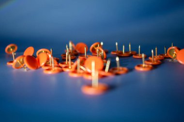 Serin mavi bir yüzeye serpiştirilmiş parlak turuncu raptiyeler. Göz alıcı karşıtlık bloglar, planlamacılar, okul temaları veya yaratıcı ofis görselleri için mükemmel