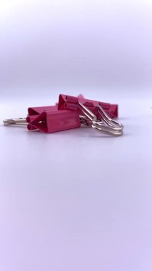 Beyaz arka planda pembe ataçlar ve mor raptiyeler. Metalik dokuları ve canlı renkleri vurgulayan renkli kırtasiye bileşimi