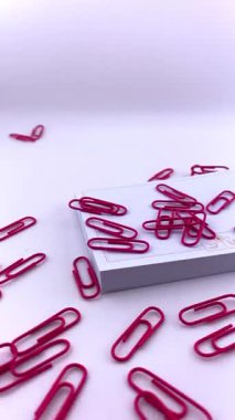 Kırmızı ataçlar ve mor raptiyeler beyaz bir yüzeye saçılmış boş bir kağıt yığınının yanında. Organizasyon ve yaratıcılık kavramları için ofis malzemelerinin renkli ve dinamik düzenlenmesi