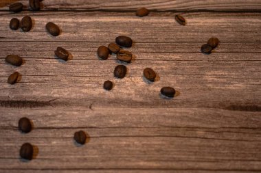 Parlak kavrulmuş kahve çekirdekleri dokuma ahşap üzerinde. Koyu kahverengi tonlar ve doğal fon kahve, yaşam tarzı ve yiyecek kavramları için ideal sıcak, topraksı ve rahat bir atmosfer yaratır..