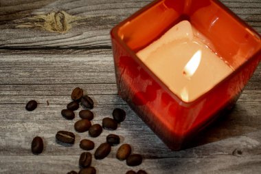 Kırsal kesimde yanan bir mumla çevrili kırmızı kare mum tutacağı, kahve çekirdekleri ile çevrili. Ilık ve dokulu ahşap rahat, davetkar ve rahatlatıcı bir atmosfer yaratır..