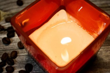 Kırsal kesimde yanan bir mumla çevrili kırmızı kare mum tutacağı, kahve çekirdekleri ile çevrili. Ilık ve dokulu ahşap rahat, davetkar ve rahatlatıcı bir atmosfer yaratır..