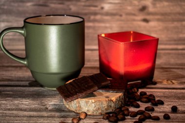 Yeşil kahve fincanı, kırmızı mum ve kırsal bir bardak üzerinde koyu çikolata, fasulyelerle çevrili. Ilık ışıklandırma ve ahşap dokular rahat ve rahat bir atmosfer yaratır..