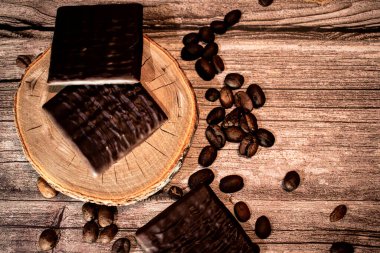 Parlak desenli çikolataya yakın çekim. Dağınık kahve çekirdekleri ve kırsal ahşap. Sıcak tonlar ve zengin dokular yemek ve yaşam tarzı için mükemmel rahat ve hoşgörülü bir atmosfer yaratır..