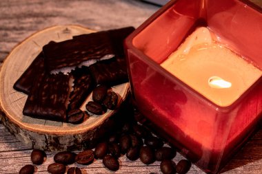 Kırsal ahşap bir dilimde çikolata naneli kırmızı parlayan mum ve dağınık kahve çekirdekleri. Sıcak, rahat, sakin bir hayat. Konfor, aroma ve rahatlatıcı bir atmosfer..