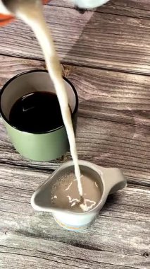 Kırsal ahşap arka planda cam bir kaba dökülen taze süt süt süt süt, süt ürünleri, kahvaltı, sağlık ve yaşam tarzı kavramları için ideal basit ve doğal bir sahne yakalıyor..