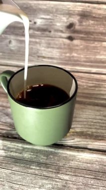 Sıcak kahve bardağına dökülen süt ahşap arka planda, kıvrımlı bir kafe havası yaratıyor, kahvaltı, yaşam tarzı veya yemek kavramları için mükemmel..