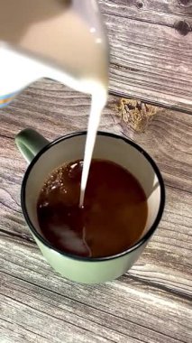 Sıcak kahve bardağına dökülen süt ahşap arka planda, kıvrımlı bir kafe havası yaratıyor, kahvaltı, yaşam tarzı veya yemek kavramları için mükemmel..