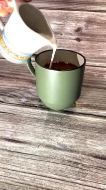 Sıcak kahve bardağına dökülen süt ahşap arka planda, kıvrımlı bir kafe havası yaratıyor, kahvaltı, yaşam tarzı veya yemek kavramları için mükemmel..