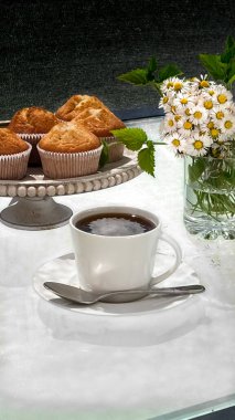 Lezzetli ev yapımı kekler ve papatyalı beyaz bir masada sıcak kahve. Kahvaltı, tatlı ya da sıcak bir mola için mükemmel..