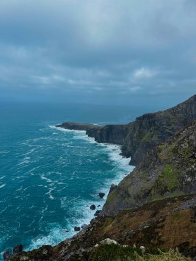 İrlanda Atlantik kayalıkları ve kıyı şeridi, dalgalar, yeşil alanlar ve vahşi Atlantik yolu boyunca fırtınalı gökyüzü..