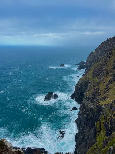 İrlanda Atlantik kayalıkları ve kıyı şeridi ile çarpan dalgalar, yeşil alanlar ve vahşi Atlantik yolu boyunca fırtınalı gökyüzü.