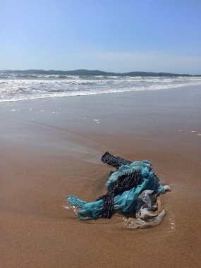 Kumsaldaki plastik atıklar okyanus kirliliğini ön plana çıkarıyor. Dalgaların ve gökyüzünün doğal güzelliğiyle çelişen karmaşık bir mavi plastik ağ kıyıya vurur. Çevresel farkındalık ve okyanus temizliği çağrısı.