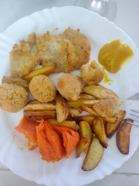 İştah açıcı bir şekilde sunulan ev yapımı tavuk, ev yapımı patates kızartması, altın hamur topları, canlı portakallı tatlı patates püresi, ve biraz hardal, sıcacık ve lezzetli bir yemek yaratıyor..