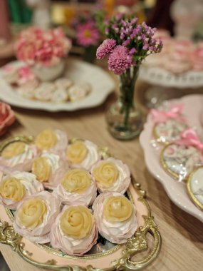 Gül şeklinde, pembe ve sarı tonlarında, süs olarak taze çiçeklerle süslenmiş, partiler ve kutlamalar için mükemmel, tatlı ve büyüleyici bir atmosfer yaratan güzel bir kapkek düzenlemesi..