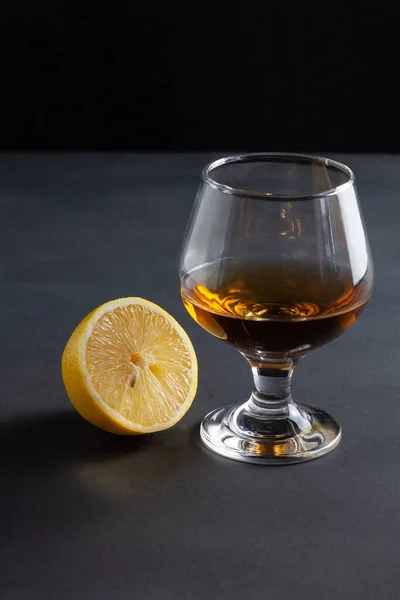 On the table is a glass of cognac. Nearby lies a cut lemon.