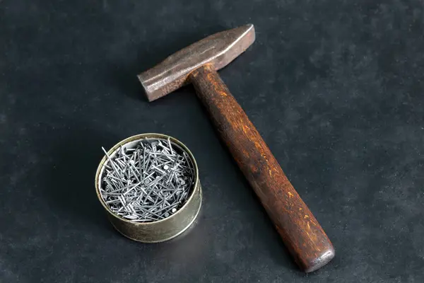 There are nails in a jar on the table. Nearby lies an old hammer. On a black background.