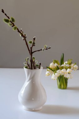 Masanın üzerinde söğüt dalları olan bir vazo var. Arkasında kardelenli bir bardak var. Seçici odak.