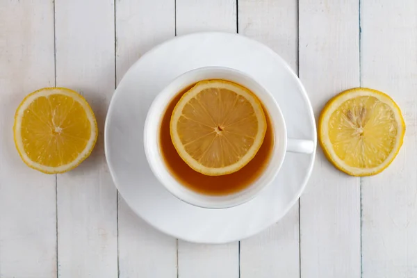 Masada bir fincan çay var. İçinde yüzen bir limon var. Yakınlarda dilimlenmiş limon dilimleri var..